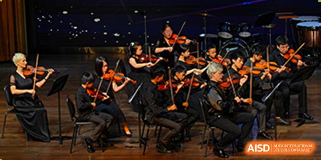 An orchestra of students from Tsinglan School performing on a stage.