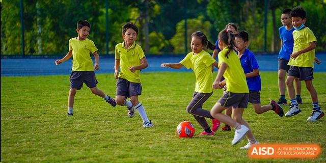 Students from Tsinglan School playing a game of soccer on a grass field.