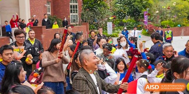 Students and teachers from Tsinglan School cheering and waving flags during a school event.
