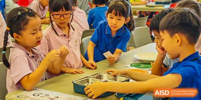A young female student from Tsinglan School looking into a metal lunchbox while seated at a table.