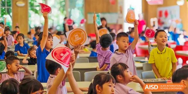 A group of young students from Tsinglan School sitting at a table and holding up paper plates they have decorated.