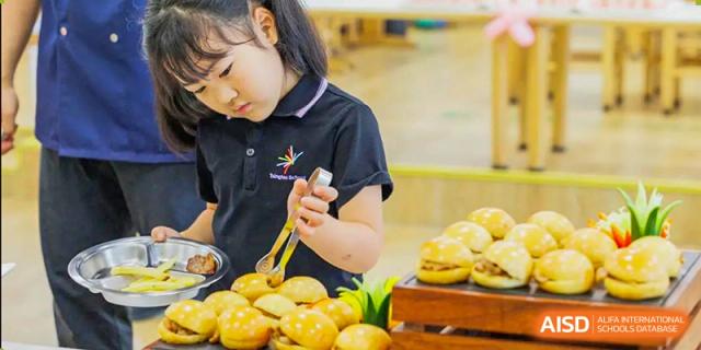 A young female student from Tsinglan School holding a pastry on a stick while looking down at a tray of pastries.
