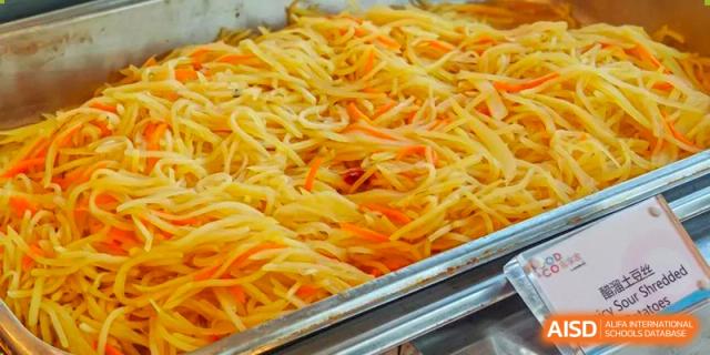 A close-up shot of shredded vegetables or noodles on a tray in the cafeteria at Tsinglan School.