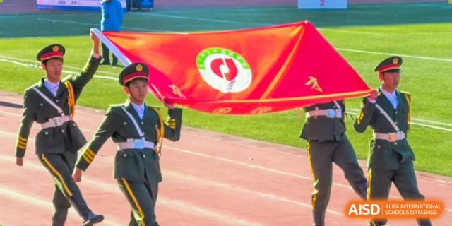 A student from Northeast Yucai Foreign Language School holds a large red flag with a circular emblem during a sports event.