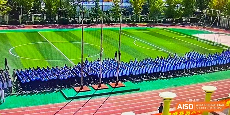 A large group of students from Northeast Yucai Foreign Language School is lined up in formation on a sports field.