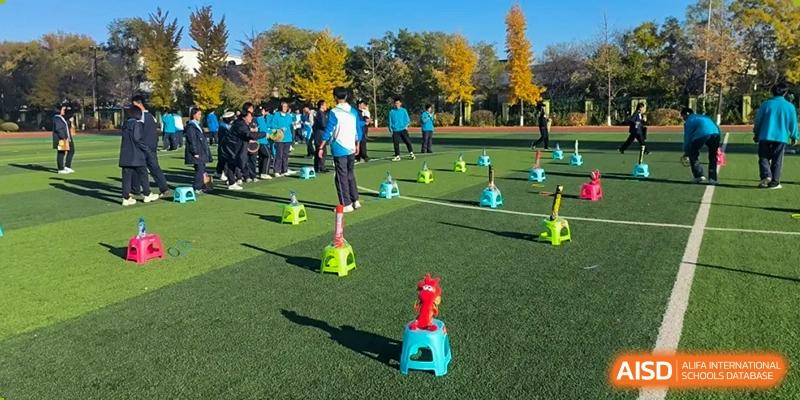 Students from Northeast Yucai Foreign Language School participate in a balance-based relay race on a field.