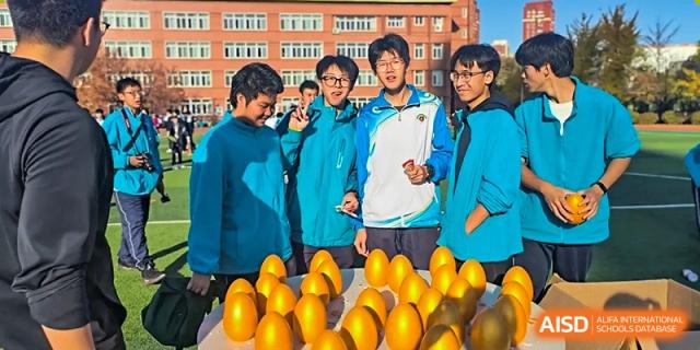 A group of students from Northeast Yucai Foreign Language School stands with large yellow, egg-shaped objects.