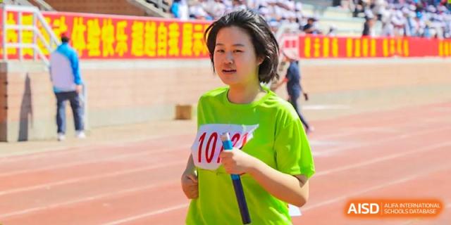A female student from Northeast Yucai Foreign Language School with a race bib smiles and stands on a running track.