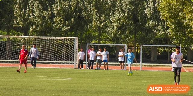 A group of students from Northeast Yucai Foreign Language School plays soccer on a field with a goal in the background.