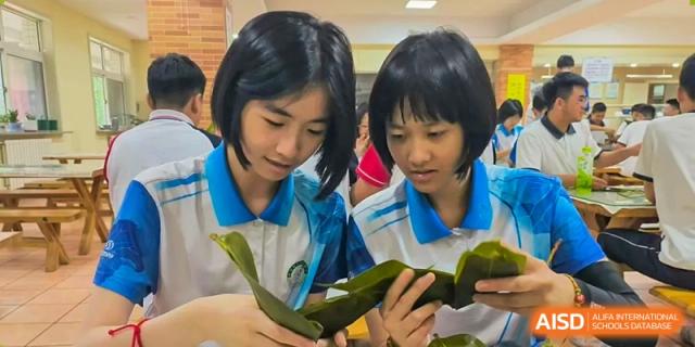 Two female students from Northeast Yucai Foreign Language School are looking at a food item wrapped in a green leaf.