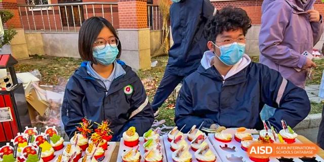 Students from Northeast Yucai Foreign Language School are trying various sweets and food items from a small buffet.