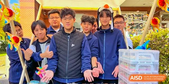 A group of students from Northeast Yucai Foreign Language School stands with their hands out, looking at something on a table.