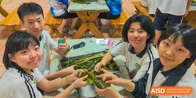 A group of students at Northeast Yucai Foreign Language School is making traditional food by wrapping it in green leaves.