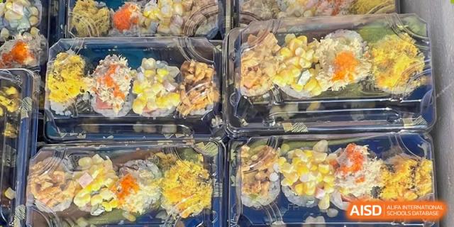 Boxes of sushi or other small food items are arranged on a table at an event for Northeast Yucai Foreign Language School.