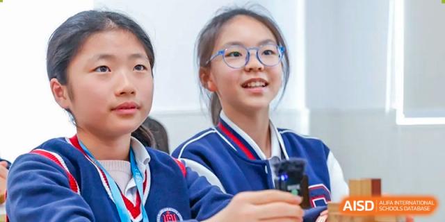 A close-up of a happy female student from Shanghai Foreign Language School Affiliated to SISU with glasses, wearing a blue and white uniform jacket.