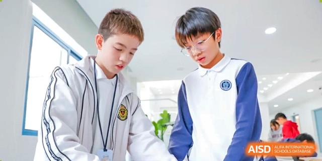 Two male students from Shanghai Foreign Language School Affiliated to SISU in white and blue uniforms collaborating and discussing a project.