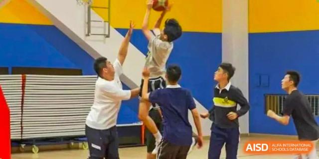 Students and adults playing basketball in a gym, with one player jumping up to shoot the ball, representing sports at the Shanghai Foreign Language School Affiliated to SISU.