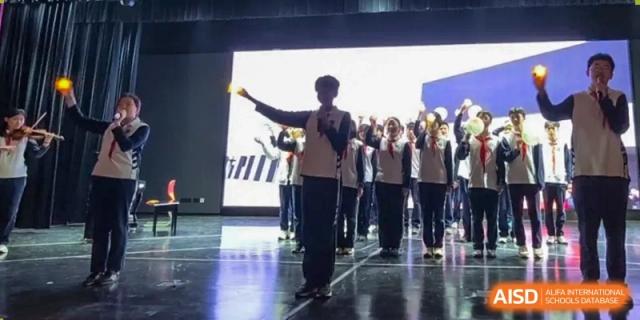 A student from Shanghai Foreign Language School Affiliated to SISU singing or performing on a stage with a group of students in uniform standing behind them.