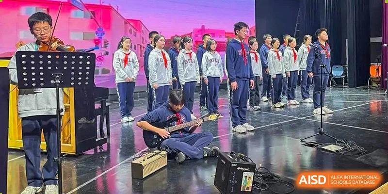 A student from Shanghai Foreign Language School Affiliated to SISU playing an electric guitar on the ground during a stage performance, with other students standing behind.