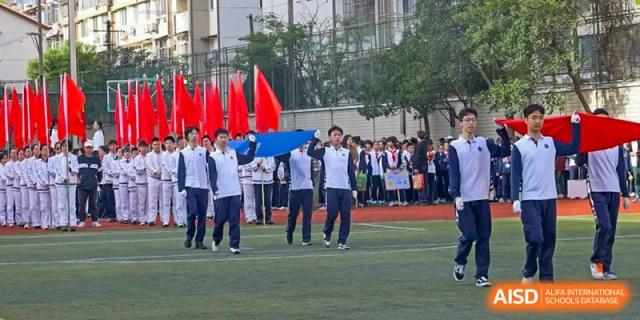 Students from Shanghai Foreign Language School Affiliated to SISU participating in an outdoor sports day or parade, carrying a blue canopy.