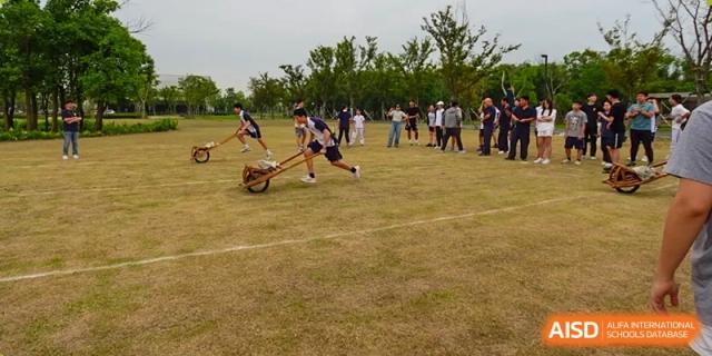 Students from Shanghai Foreign Language School Affiliated to SISU participating in an outdoor sports day game, possibly a wooden scooter or chariot race.