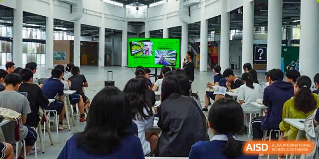 Students at Shanghai Foreign Language School Affiliated to SISU watching a presentation or video on a large screen in an indoor gathering space.
