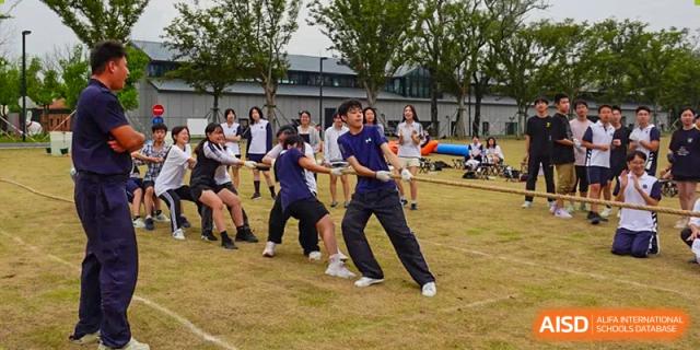 Students from Shanghai Foreign Language School Affiliated to SISU participating in a team-based sport or tug-of-war game on a grass field during a school event.