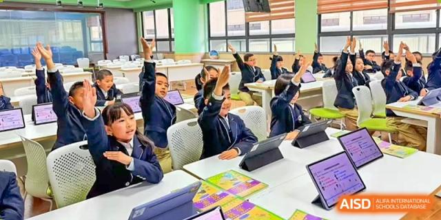 A group of students is raising their hands to ask a question or answer a question in a brightly lit classroom at Shanghai Shangde Experimental School.