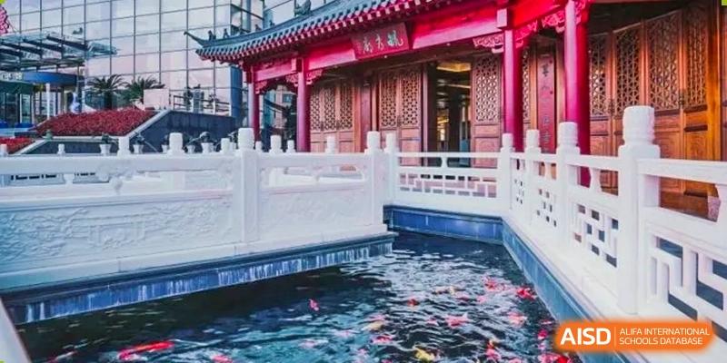 A traditional Chinese building with a red roof sits next to a koi pond at Shanghai Shangde Experimental School.