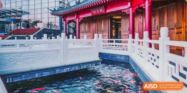 A traditional Chinese building with a red roof sits next to a koi pond at Shanghai Shangde Experimental School.