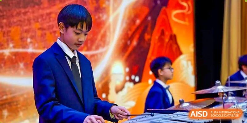 Students are playing instruments on a stage with a bright screen in the background at Shanghai Shangde Experimental School.
