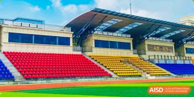 This shows an empty sports stadium with red and yellow seating at Shanghai Shangde Experimental School.