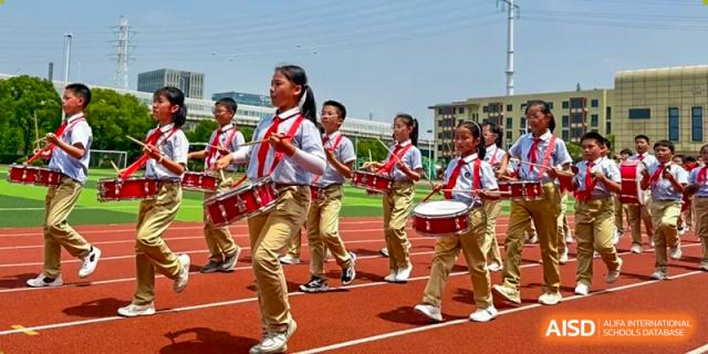 Students in a marching band are playing drums on a track at Shanghai Shangde Experimental School.