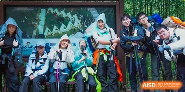 A group of students wearing rain ponchos are posing for a photo outdoors at Shanghai Shangde Experimental School.