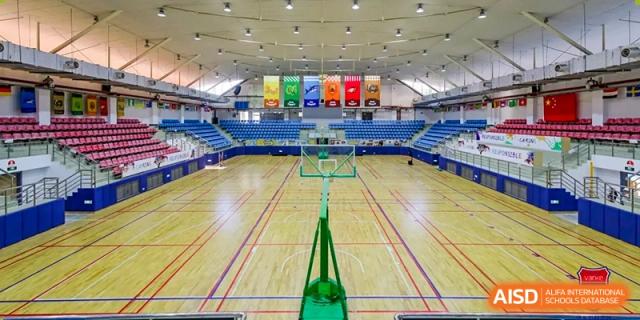 Vanke School Pudong indoor basketball court and gymnasium with seating bleachers and championship banners.