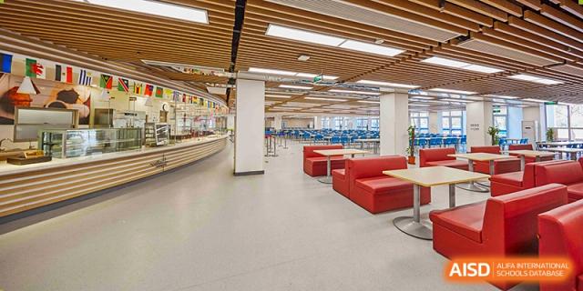 The cafeteria or dining hall at Vanke School Pudong, featuring light wooden ceilings, scattered tables, and red booth seating.