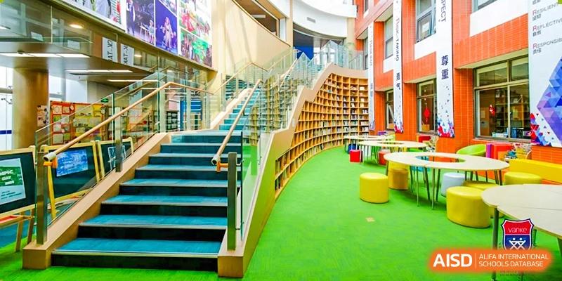 A multi-level staircase and library area at Vanke School Pudong with bright green carpet and wood shelving, showing a curved architectural design.