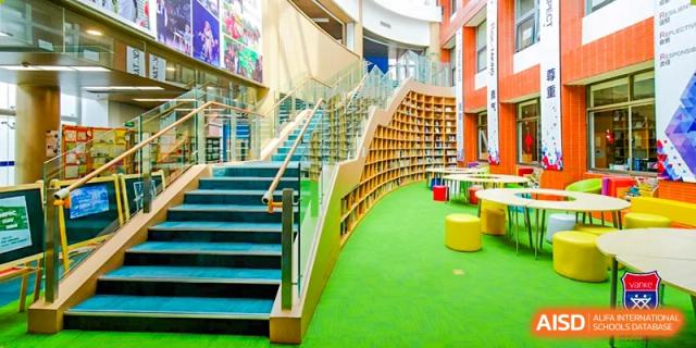 A multi-level staircase and library area at Vanke School Pudong with bright green carpet and wood shelving, showing a curved architectural design.