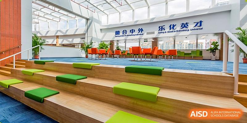 A common or gathering area at Vanke School Pudong with wooden tiered seating, comfortable green and orange cushions, and large windows.