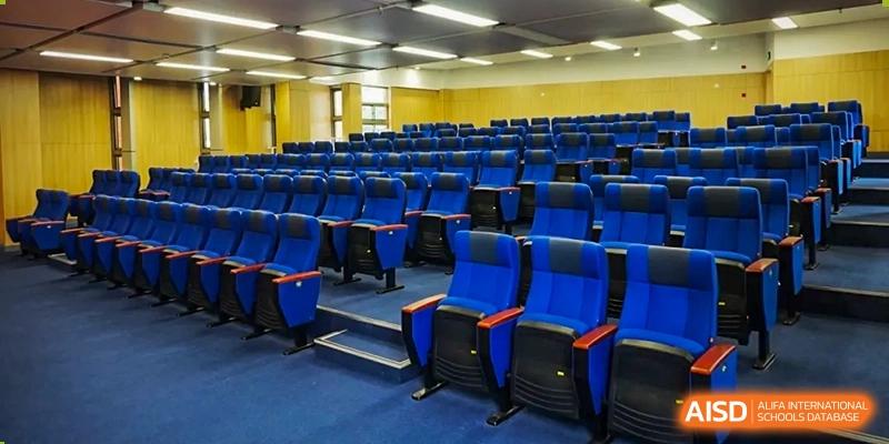 A large auditorium or lecture hall at Vanke School Pudong with multiple rows of dark blue seating and a stage area.