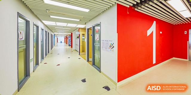 A clean, well-lit interior hallway at Vanke School Pudong with white walls, red accents, and a wide doorway.