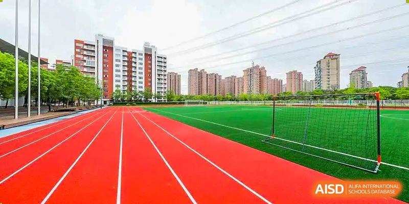 The outdoor red running track and turf sports field at Vanke School Pudong with apartment buildings visible in the background.