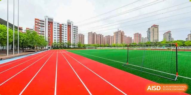 The outdoor red running track and turf sports field at Vanke School Pudong with apartment buildings visible in the background.