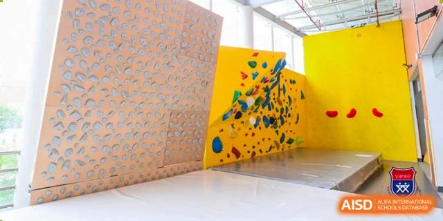 A climbing wall area at Vanke School Pudong featuring colorful, textured panels with various handholds for bouldering.