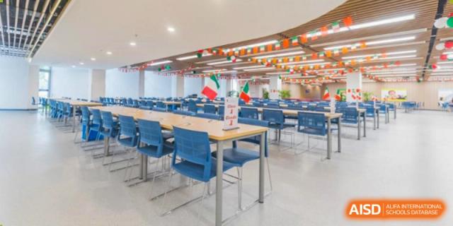 A section of the spacious Vanke School Pudong cafeteria with light-colored tables, blue chairs, and festive flags hung from the ceiling.