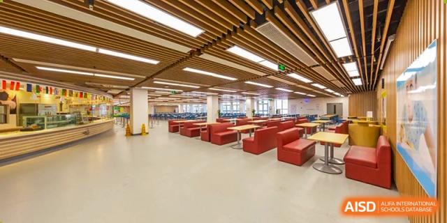 The modern dining area at Vanke School Pudong, featuring warm wooden ceilings, an open layout, and comfortable red booth seating.