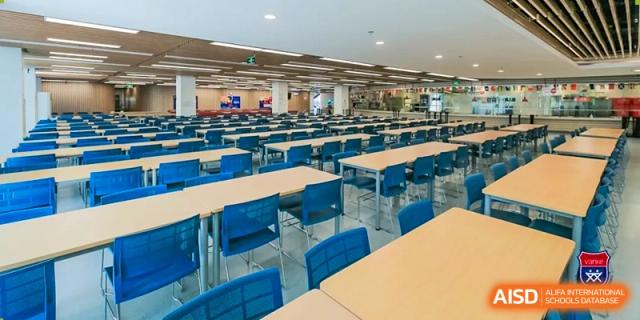 A wide view of the main cafeteria hall at Vanke School Pudong, equipped with many tables and blue chairs for student meals.