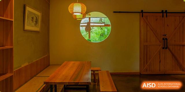 An interior seating area at Wuhan Foreign Languages School International Division featuring a circular window with a view of greenery, and a wooden table.