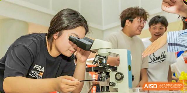 A female student from Suzhou North America High School is looking through a microscope in a science lab.