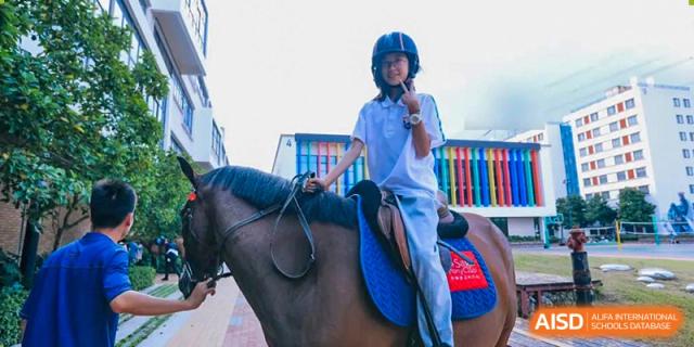 A student from Suzhou North America High School is riding a horse, wearing a helmet and giving a thumbs-up.